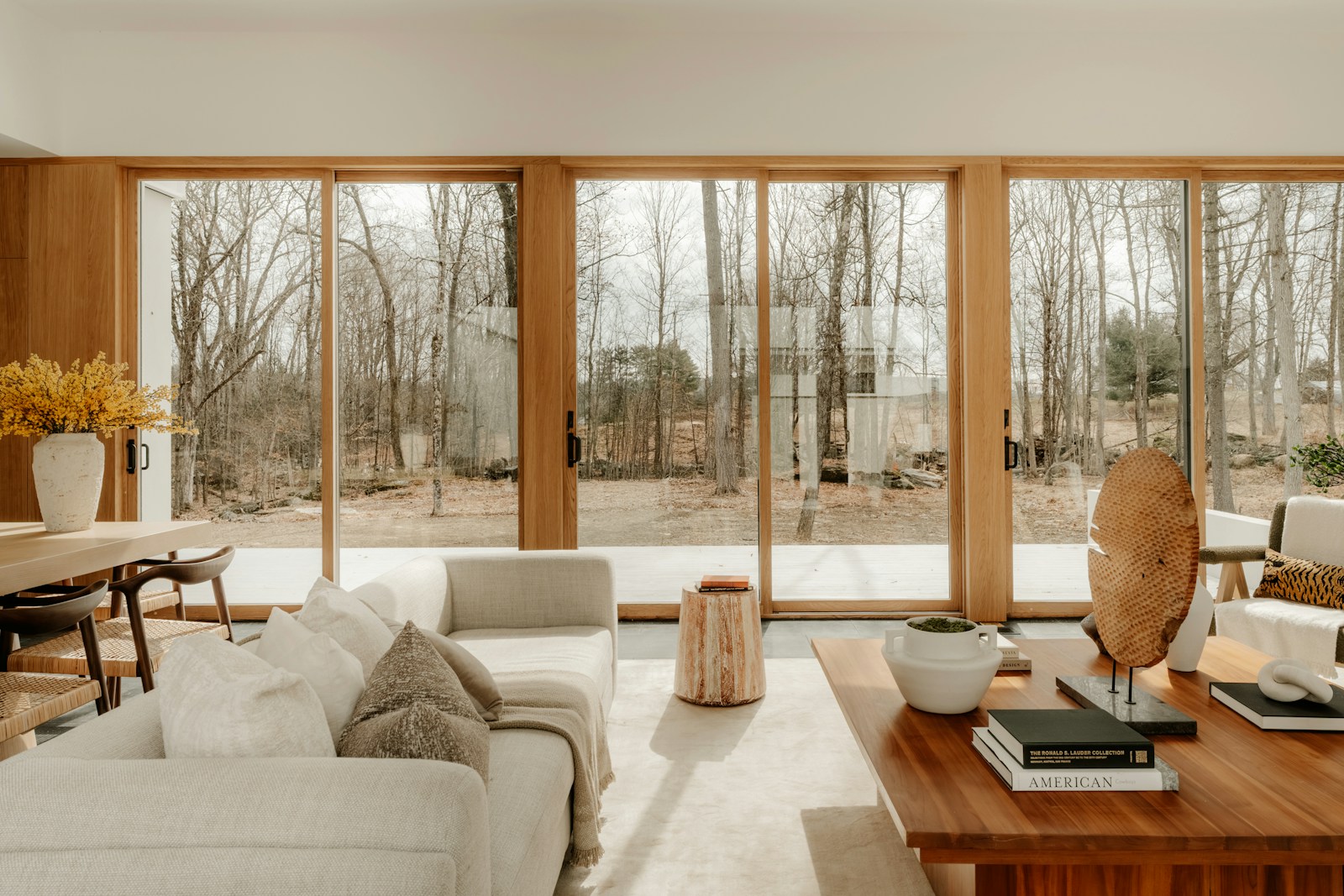 A sunlit living room with oak windows, cream sofas, and a view of the trees